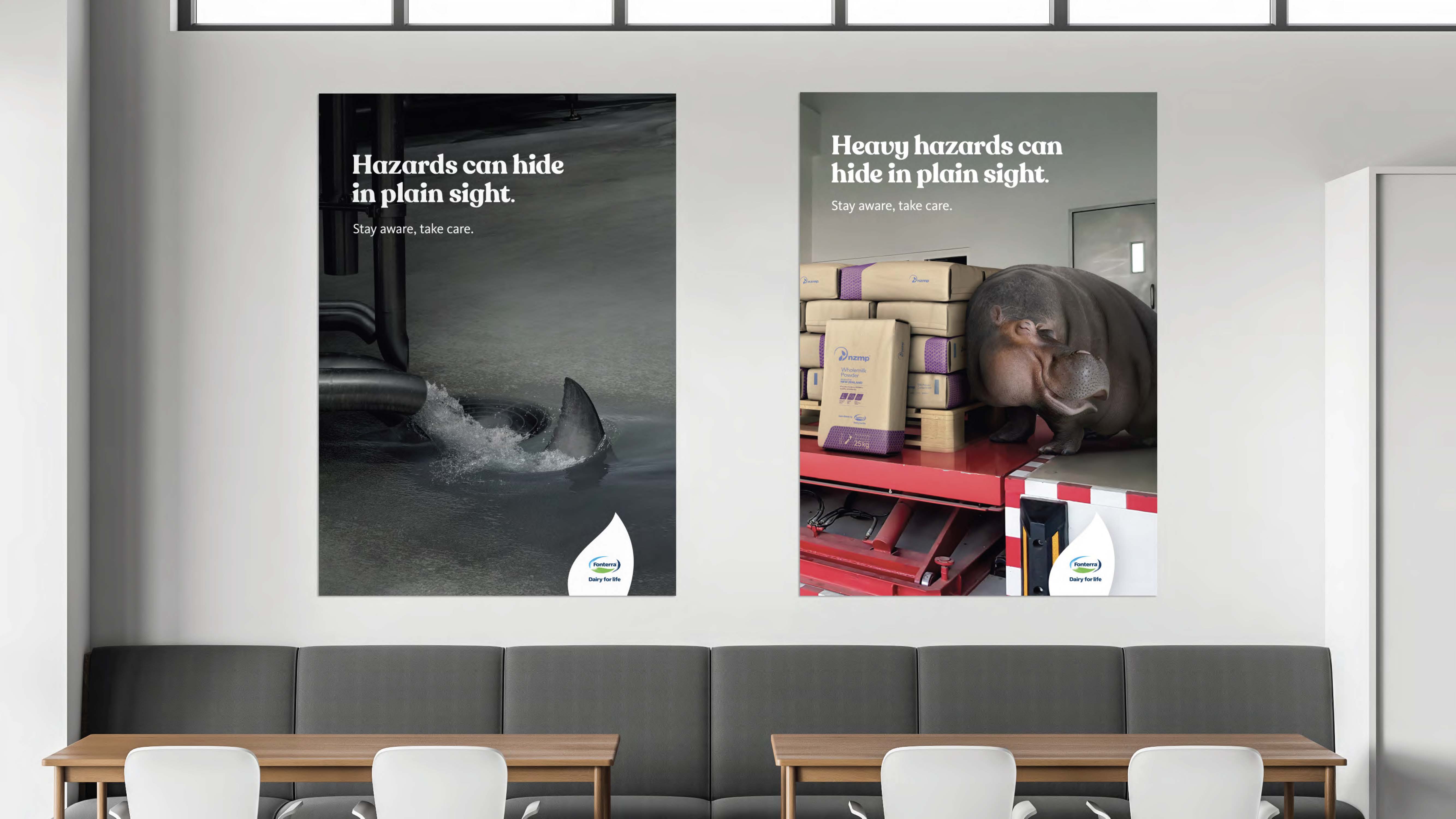 Two Danger in Disguise posters mounted in a Fonterra meeting room: 'Hazards can hide in plain sight' with a shark fin emerging from a factory pipe, and 'Heavy hazards can hide in plain sight' with a hippo lurking among stacked milk-powder bags.