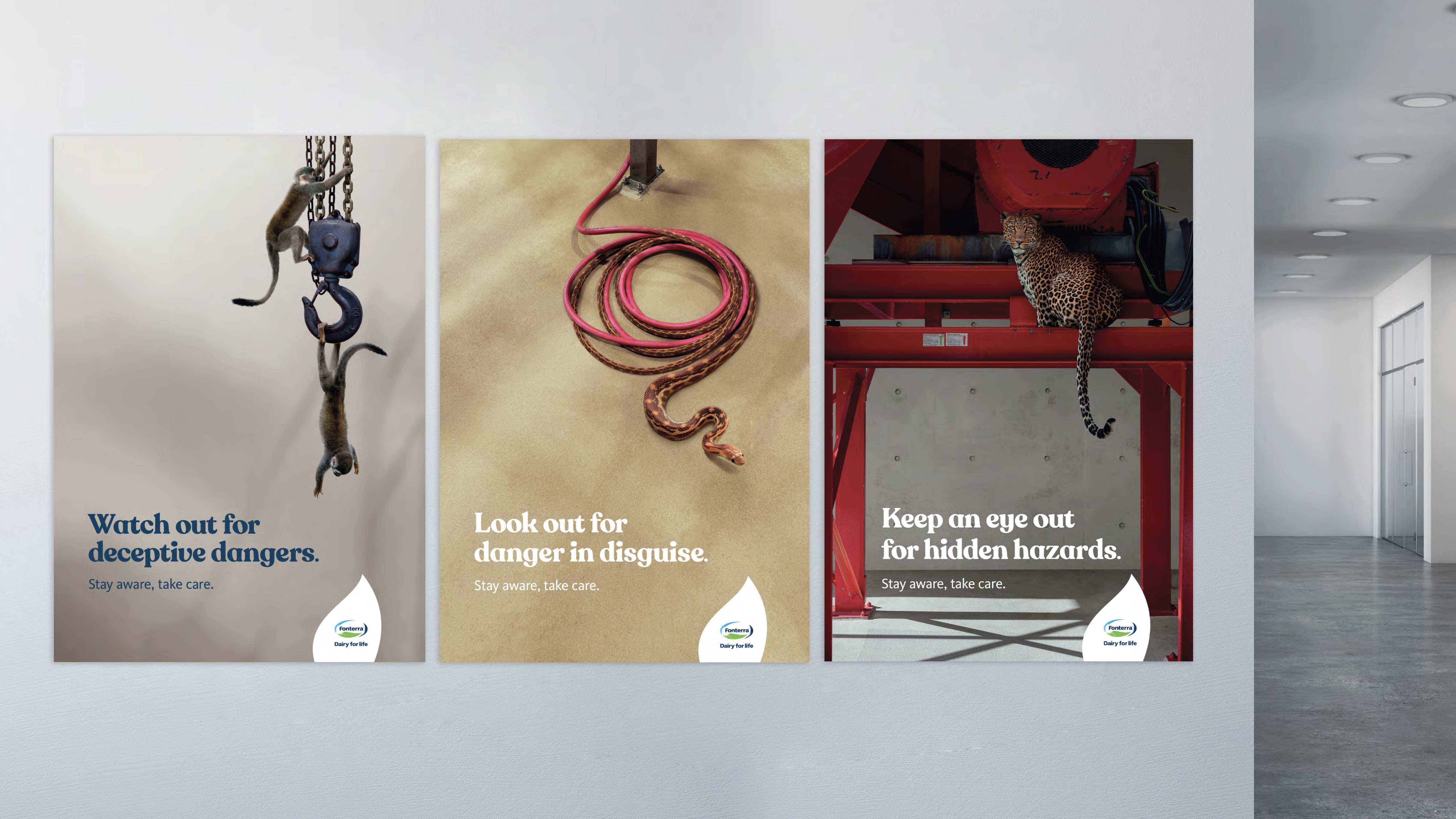 Danger in Disguise campaign installation: three Fonterra workplace-safety posters mounted on a wall, each pairing factory machinery with hidden animals — meerkats, snake, leopard — under the lines 'Watch out for deceptive dangers,' 'Look out for danger in disguise,' 'Keep an eye out for hidden hazards.'