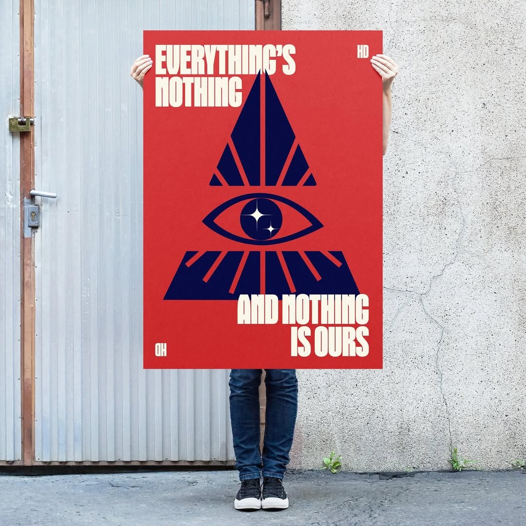 Heart Department in-situ poster — a person holds an 'EVERYTHING'S NOTHING / AND NOTHING IS OURS' brand poster against a graffitied alley wall, with the all-seeing-eye-and-pyramid mark front and centre.